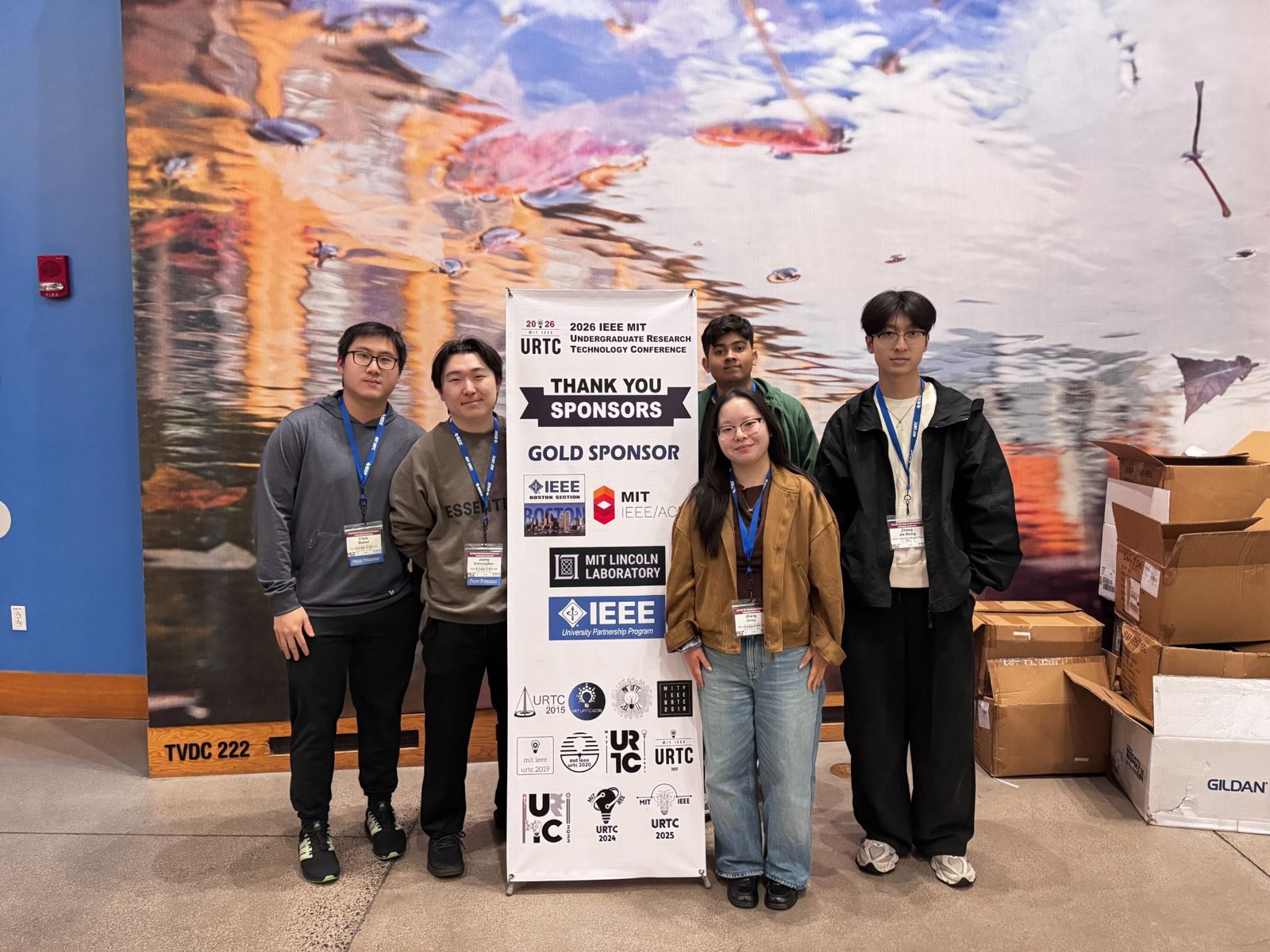 CCNY BEAT+ students at IEEE URTC 2026 in front of the conference sponsor banner